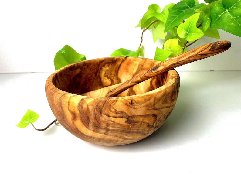 Bol din lemn de măslin cu o lingură asortată, lângă o plantă verde